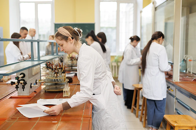 A group of students wearing white coats work in a chemistry lab.