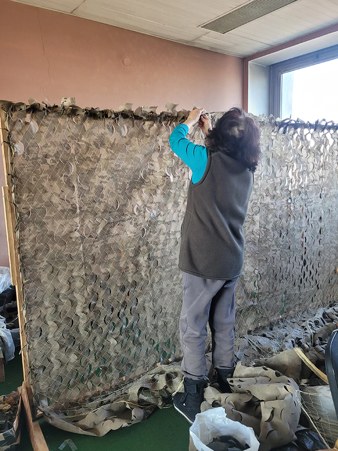 A woman works on building camouflage netting.