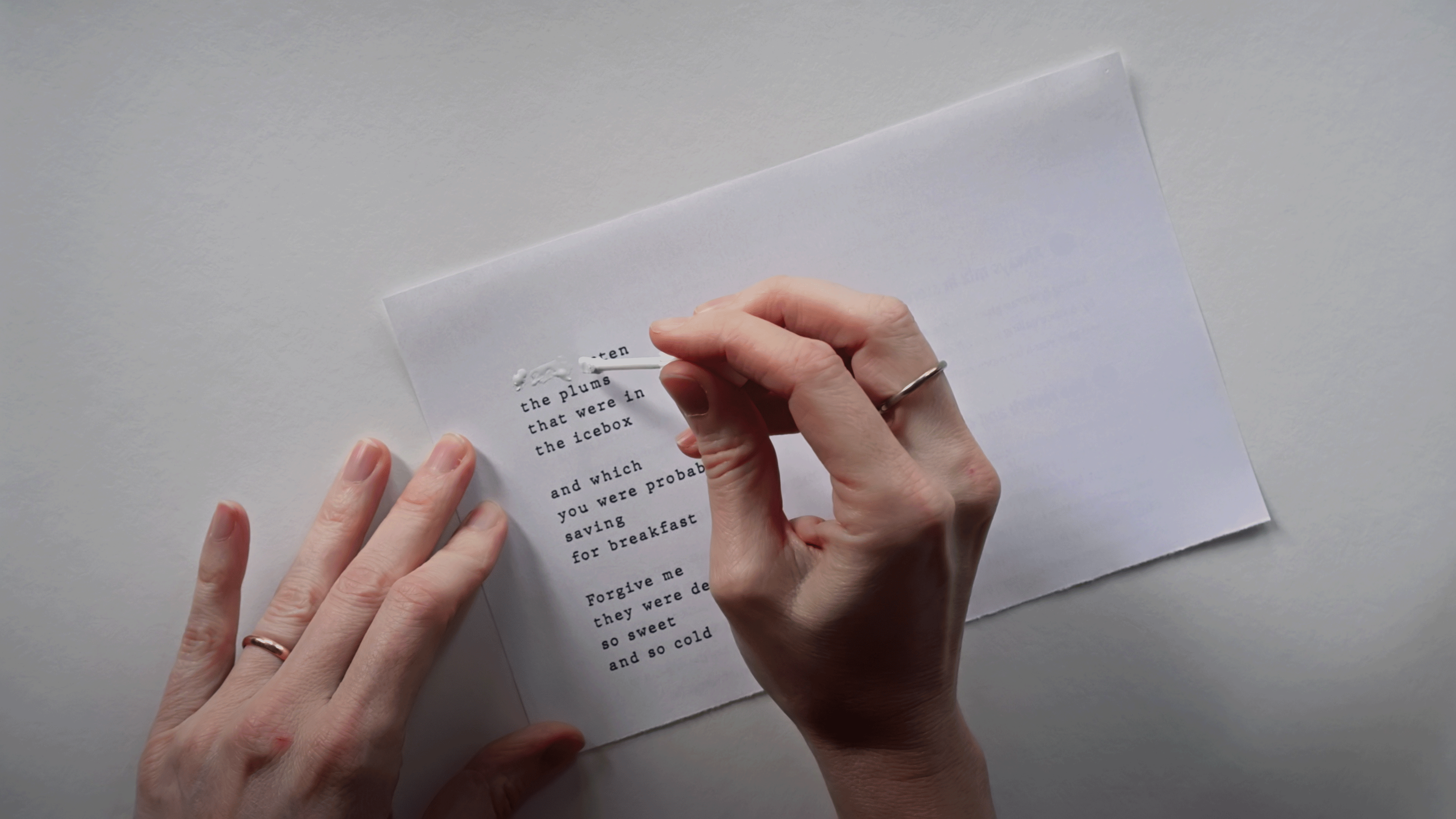Two hands, one holding a paper while the other applies whiteout to text set like a poem.