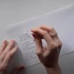 Two hands, one holding a paper while the other applies whiteout to text set like a poem.