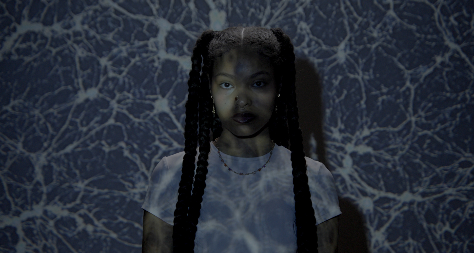 Woman with braids standing in front of a projection of cosmos.