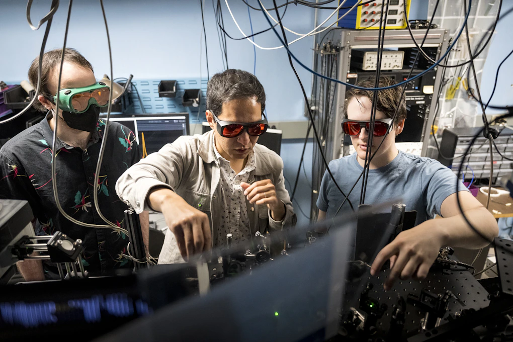 A photo of Axel and two students working on equipment with protective goggles on