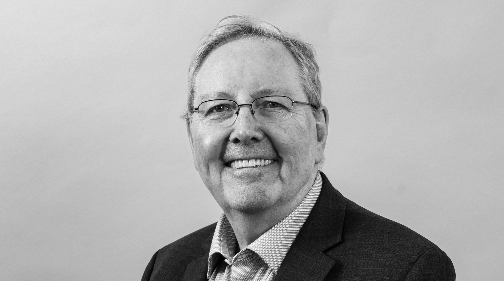 Portrait of Peter Littlewood on a plain backdrop, wearing a suit and smiling.