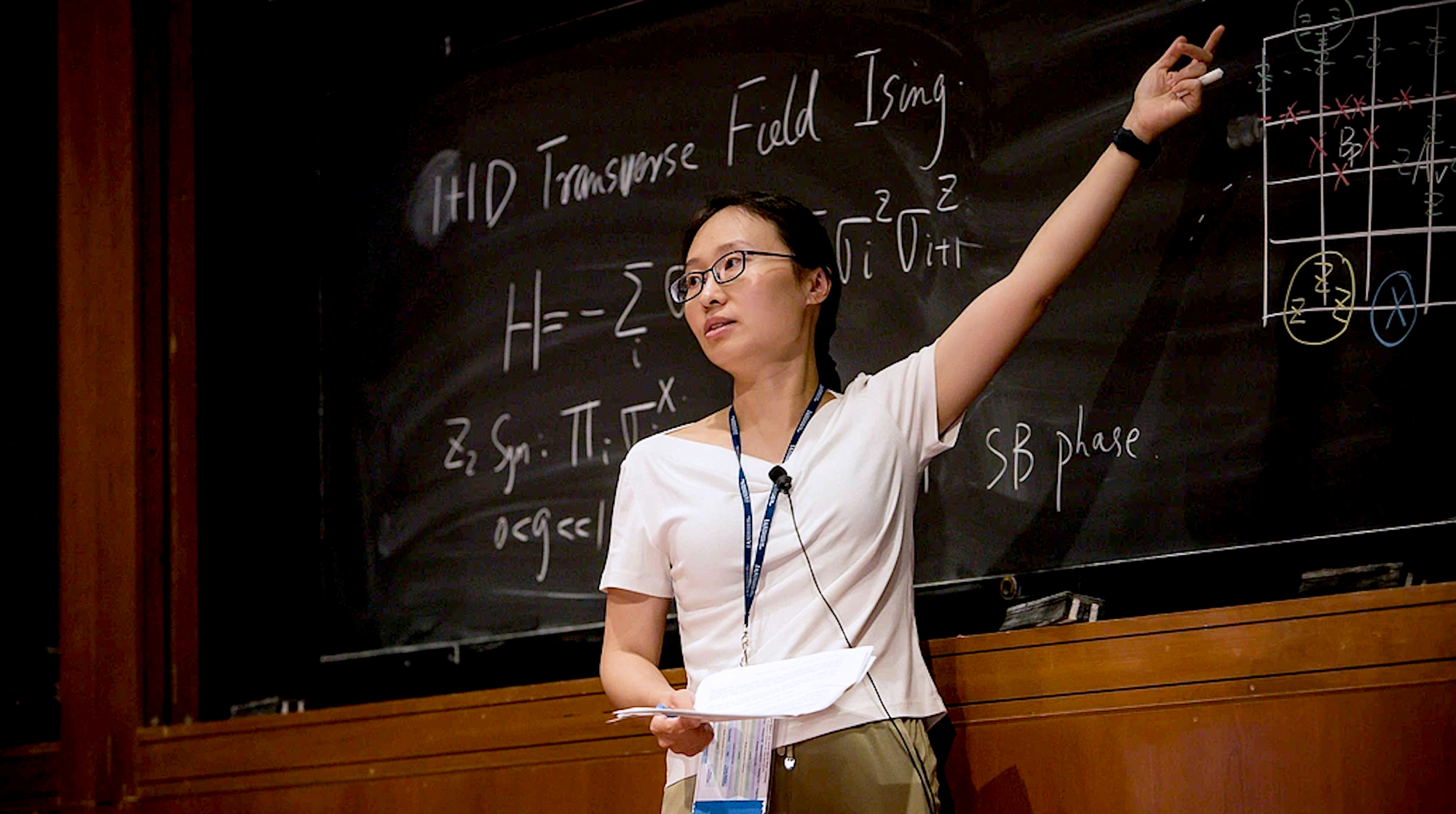 A photo of Xie Chen presenting in front of a large chalkboard.