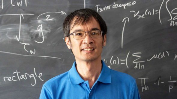 Mathematician Terence Tao poses in front of a blackboard filled with mathematical equations.