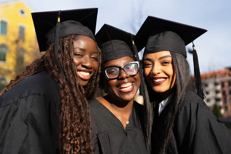 Three young women wearing graduation gowns and caps are smiling at the camera on graduation day.