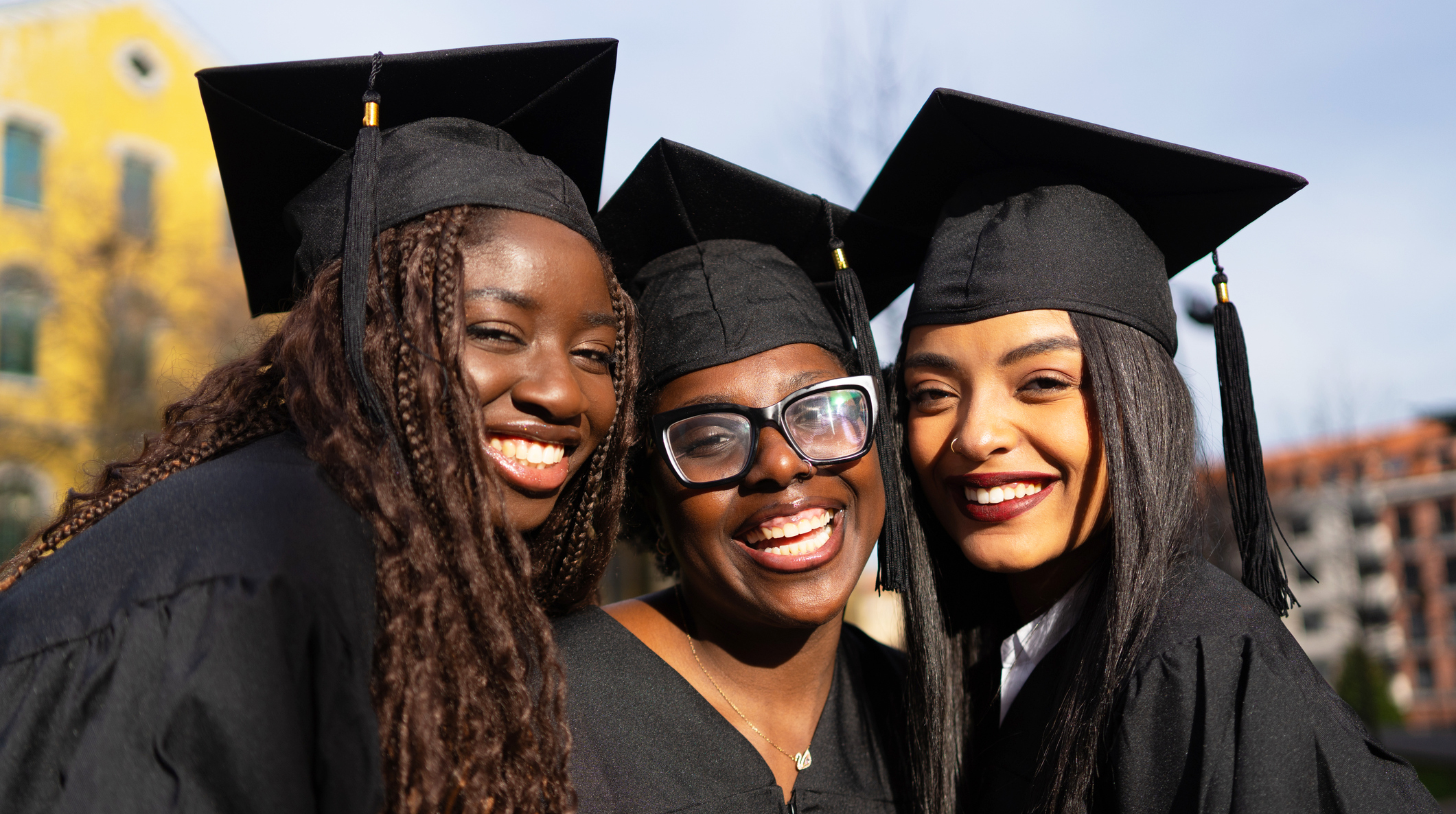 Three young women wearing graduation gowns and caps are smiling at the camera on graduation day.