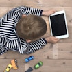 Top view header image with child laying down on the floor watching a movie on his tablet instead of playing with his toy cars