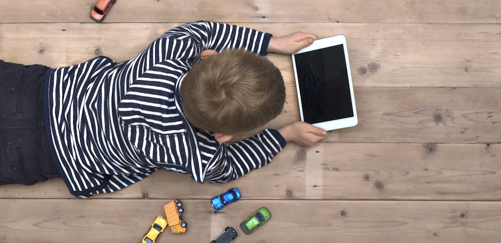 Top view header image with child laying down on the floor watching a movie on his tablet instead of playing with his toy cars