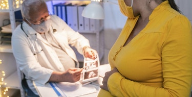 Senior doctor gynecologist doing periodical medical exam of a young pregnant woman in her third trimester.