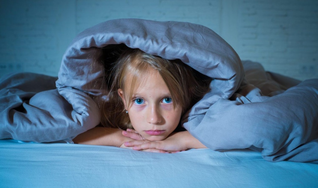 Cute little caucasian girl lying in bed covering her head with blanket feeling exhausted and sleepless suffering from insomnia Depression Stress in Children Emotional and Sleeping Disorders concept.