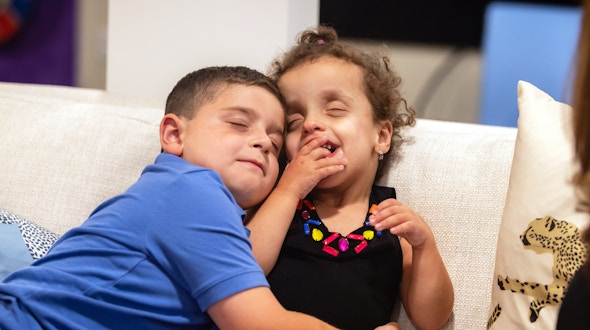 Two children cuddle on a sofa.