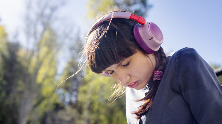 Photo of a A neurodivergent teenage girl (with autism and Rett syndrome) wearing bright headphones and smiling while sitting next to her personal care assistant at home.