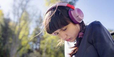 Photo of a A neurodivergent teenage girl (with autism and Rett syndrome) wearing bright headphones and smiling while sitting next to her personal care assistant at home.