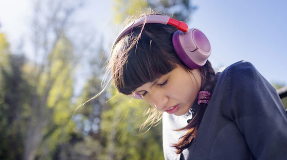 Photo of a A neurodivergent teenage girl (with autism and Rett syndrome) wearing bright headphones and smiling while sitting next to her personal care assistant at home.