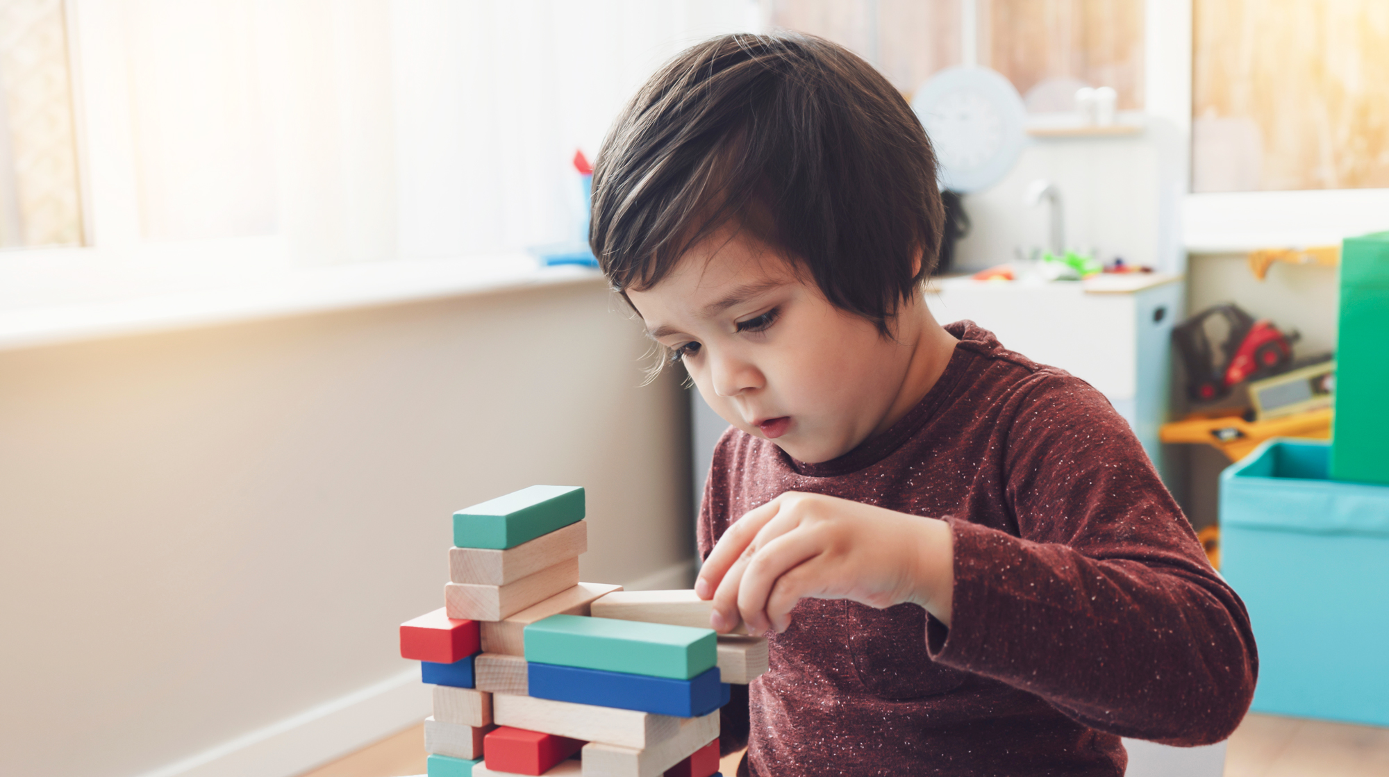 A candid shot of cheerful little boy plays colorful wooden blocks in play room.