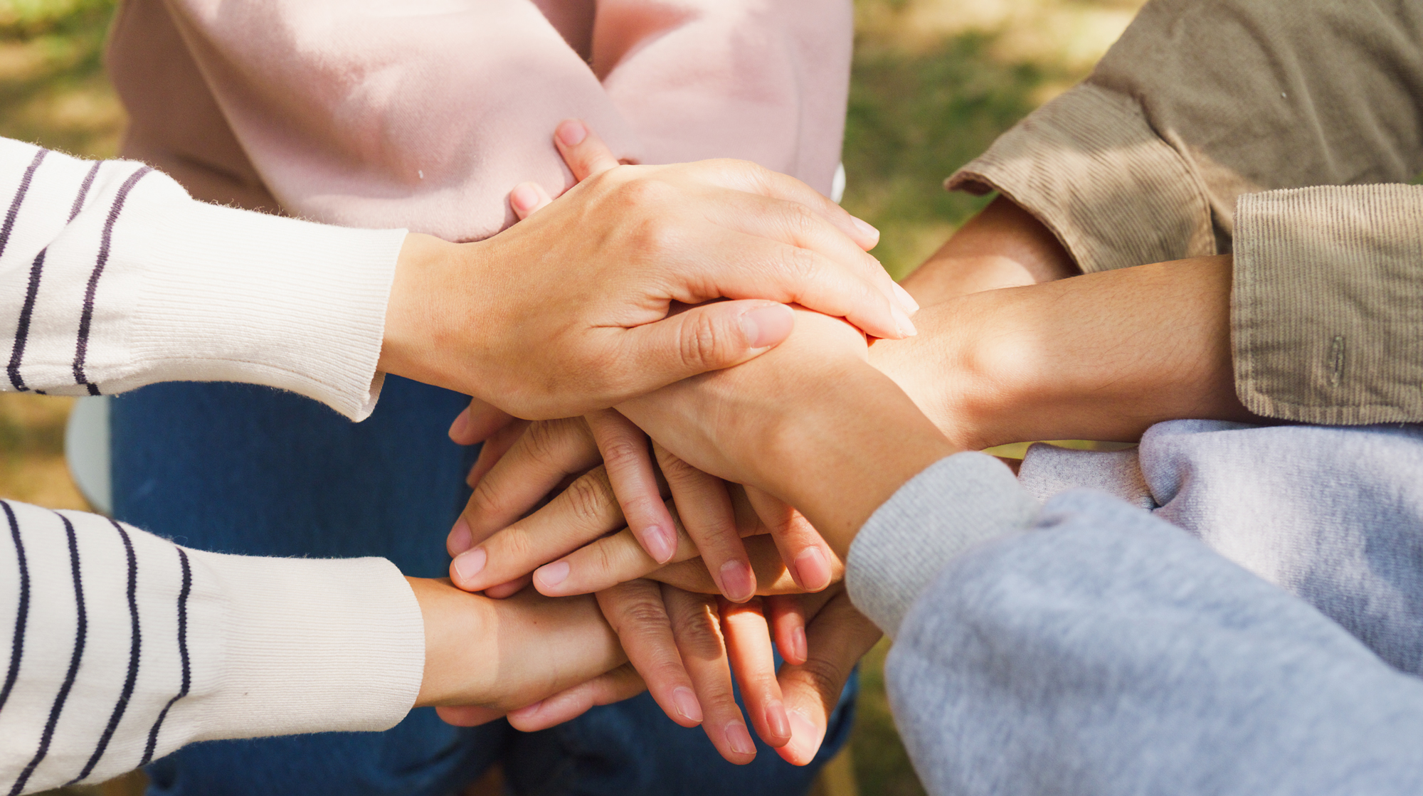 A close-up of diverse multiracial men and women group with stacking hands on top of each other, suggestive of a support group.