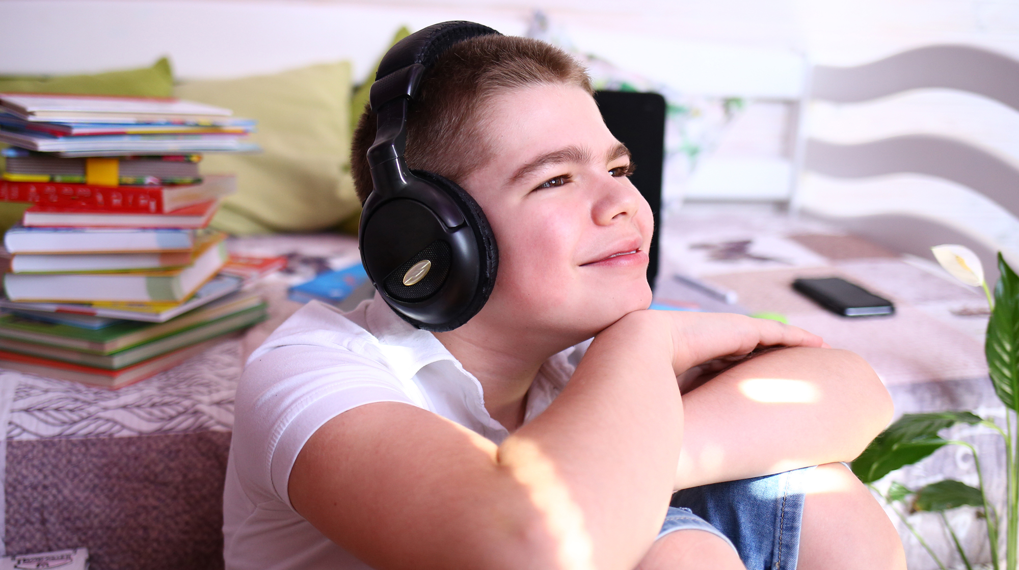 Portrait of smiling boy wearing headphones with books sitting on the table behind him.