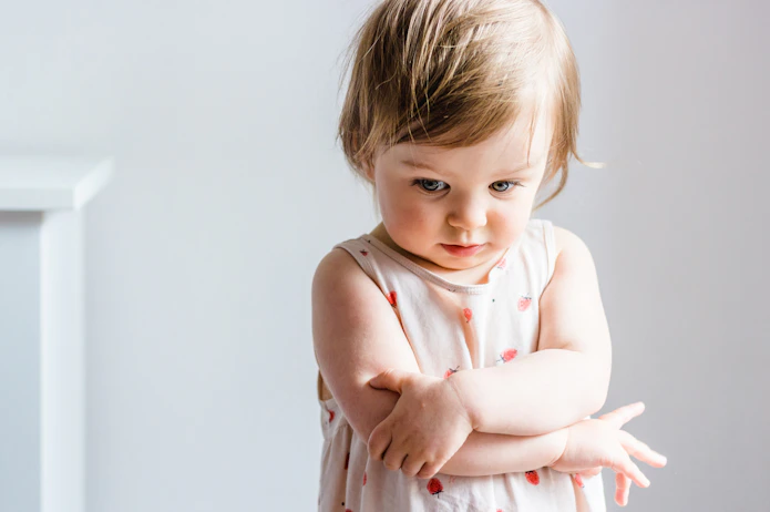 Sad or angry toddler baby girl looking down with her arms crossed.