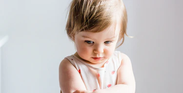 Sad or angry toddler baby girl looking down with her arms crossed.