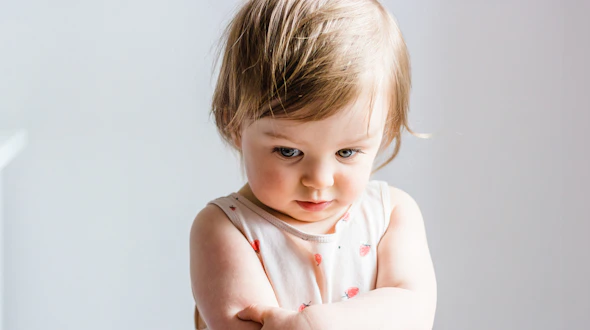 Sad or angry toddler baby girl looking down with her arms crossed.