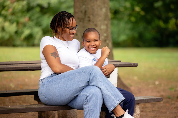 A photo of a smiling young boy with a smiling woman sitting on a bench.