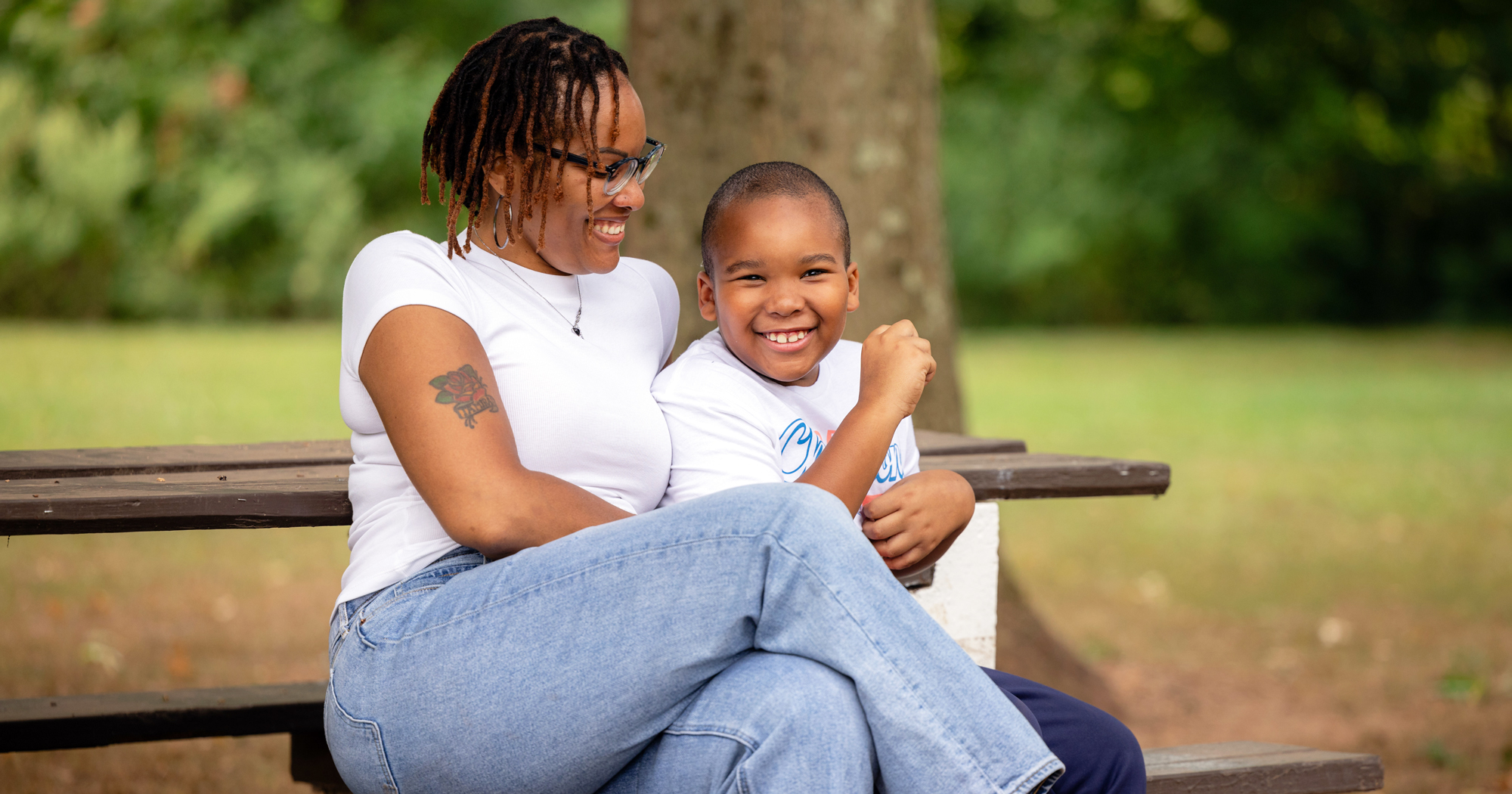 A photo of a smiling young boy with a smiling woman sitting on a bench.
